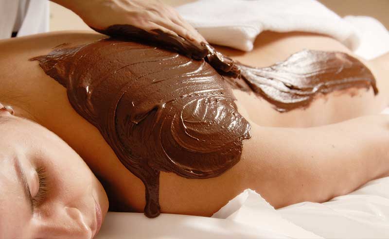Csokoládé és kakaóvaj masszázs, a relaxáló hölgy hátán a szépen felkent csokoládé látszik