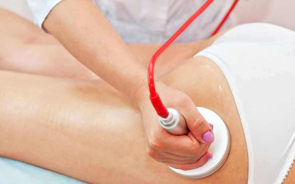 Alakformáló mélymasszázs gyógymasszőrtől, egy női felsőcombon, speciális ultrahangos készülék segítségével